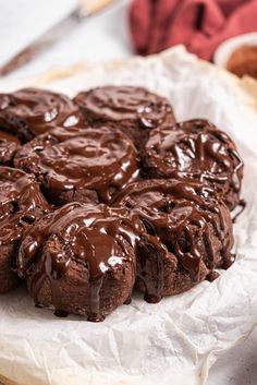 chocolate donuts are sitting on top of wax paper with icing drizzled over them