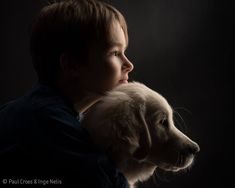 a young boy holding a white puppy in his arms and looking off into the distance