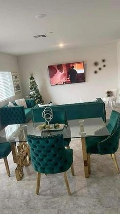 a dining room with green velvet chairs and a glass table in the middle, surrounded by white couches