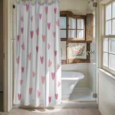 a shower curtain with pink hearts on it in front of a bathtub and window