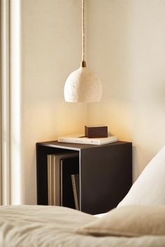 a lamp hanging over a bed next to a night stand with a book on it