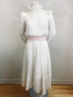 "What a romantic Gunne Sax / Boho style dress! - 1970's - \"Act 1\" label - Gunne Sax / Boho style - Midi length - White crinkled cotton gauze  - White light weight cotton lining - Victorian style lace collar - White lace trim on neckline, shoulders, bust, and sleeve cuffs - Bishop sleeves with lace cuffs - 5 pearl buttons on each sleeve - 1 pearl button closure on back of neck - Two belt loops on side - Pink sash belt - Elastic waist - Ruffle panel on bottom of skirt - Polyester zipper Measurem White Vintage Prairie Dress For Daywear, Vintage Cream Prairie Dress For Garden Party, Spring Victorian Dress For Vintage Fashion, White Vintage Victorian Dress For Spring, 1970s Style White Maxi Dress, Vintage White Victorian Dress For Spring, Vintage Fitted White Prairie Dress, Fitted Vintage White Prairie Dress, Fitted White Vintage Prairie Dress