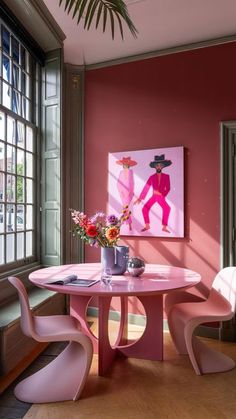 a pink table and chairs in front of a window with a painting on the wall