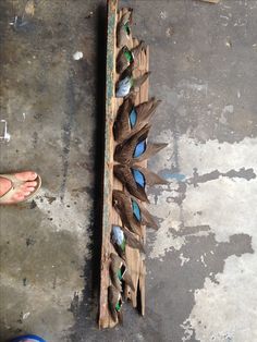 a piece of wood that has some blue and green feathers on it, sitting next to a person's foot