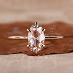 an oval shaped diamond ring sitting on top of a brown piece of leafy material