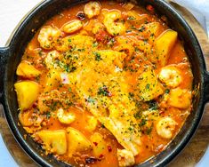 a skillet filled with shrimp, potatoes and tomato sauce