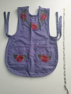 a blue and white checkered vest with roses on it next to a measuring tape