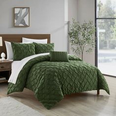 a bed with green comforter and pillows in a room next to a window,