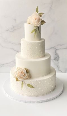 a three tiered white wedding cake with flowers on the top and bottom, sitting on a marble table