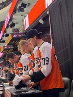 three men in orange and white jerseys standing at a table