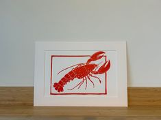 a red and white print of a lobster on a wooden shelf next to a wall