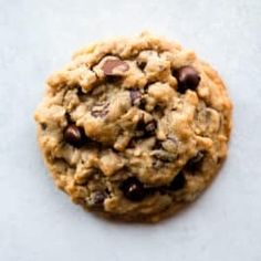 an oatmeal cookie with chocolate chips on top sitting on a white surface