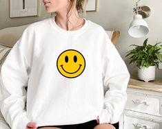 "Smiley Faces Sweatshirts, Cute Smiley Face Sweater, Smiling Emoji Tee, Positive Vibes,Happy Face, Retro Smiley Face Shirt,Emoji Face Shirts Welcome to the different, crazy and colorful world of ORANGE WORLD :) PRODUCT DETAILS Collar, shoulders, armholes, cuffs and hem double-needle stitched  -  1 x 1 rib with spandex Features a crewneck -  Relaxed fit - Unisex -  50% cotton 50% polyester HOW TO ORDER 1- Please review all photos, 2- Choose your size and color from the drop-down menus, 3- Click the \"add to cart\" button, 4- Go back for another product and go to 1.2.3. repeat the steps. CARE INSTRUCTIONS -  Turn it upside down and machine wash at low temperature on the delicate programme. -  Dry on a low heat setting -  Do not bleach -  Do not dry clean -  Do not iron directly on the design White Relaxed Fit Top With Smiley Face, White Smiley Face Top With Relaxed Fit, White Crew Neck Top With Smiley Face, White Smiley Face Crew Neck Top, Smiley Face Sweater, Smiling Emoji, Sweatshirts Cute, Retro Smiley Face, Smiley Face Tshirt