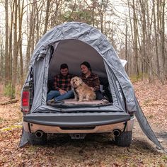 two people sitting in the back of a truck with a dog