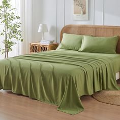 a bed with green sheets and pillows in a room next to a plant on the floor