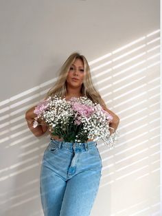 a woman standing in front of a white wall holding a bouquet of pink and white flowers