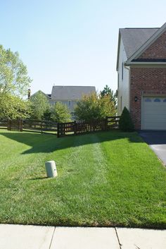 a yard with grass, fence and trash can in front of a house on a sunny day