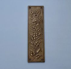 a decorative metal plaque with flowers on it's side against a light blue wall