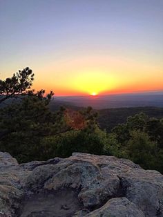 the sun is setting over some rocks and trees