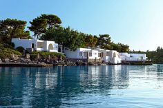 several white buildings sitting on top of a hill next to the ocean with trees in the background