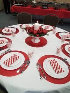 the table is set with red and white plates, silverware, and candlesticks