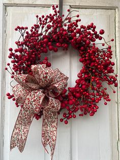 a red berry wreath hanging on the side of a white door with ribbon and bow