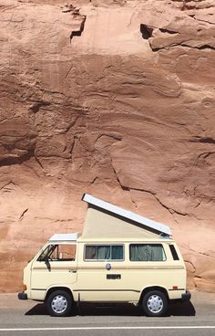 a van parked in front of a large rock formation with a camper on top