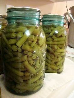 three jars filled with green beans sitting on top of a counter