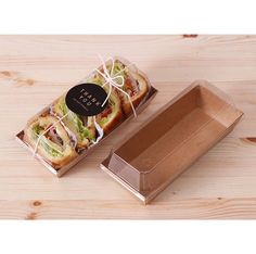 two sandwiches in a cardboard box on a wooden table next to a package with the lid open