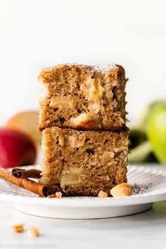 two slices of apple cake on a plate with cinnamon sticks and apples in the background