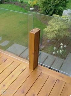 a wooden deck with glass railing next to a grassy area in the back yard,