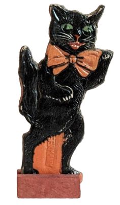 a black cat with an orange bow tie sitting on top of a piece of wood