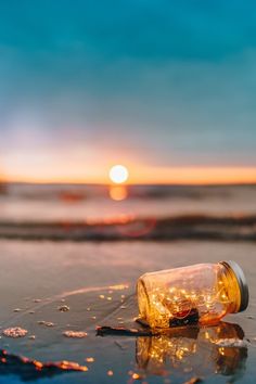 a bottle that is sitting on the sand near the ocean at sunset or sunrise time