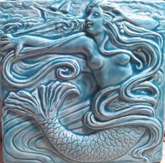 a blue ceramic tile with a mermaid on it's face and the shape of a fish