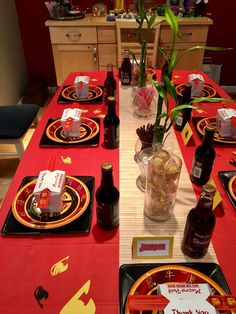 the table is set with red and gold place mats, black plates, and vases