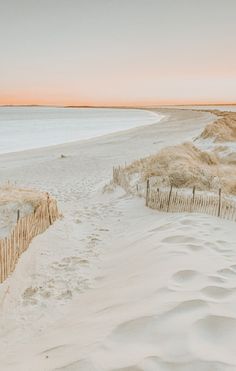 a sandy beach next to the ocean with sand dunes and fenced in area at sunset