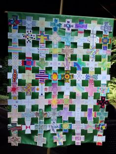 a green and white quilt hanging on a pole in front of a tree with lots of stickers all over it