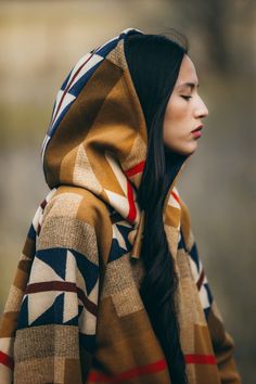 Bell-shaped hooded cloak with welt patch pockets and 3 toggle closure. Corine is 5'9" and wears size OS. Unnapped Pendleton blankets: 82% Wool, 18% Cotton. Wool Cashmere facings and Silk Rayon peachskin lining. Native American tribes traveled to Wyoming’s Medicine Bow Mountains to harvest wood for especially fine bows. In this design, stands of wood alternate with arrows that meet in the center to evoke the Medicine Bow River, an important crossing point through the Continental Divide. Expertly Native American Clothing Modern, Native American Outfit Women, Native American Traditional Clothing, Native American Style Outfits, Native American Inspired Fashion, Indigenous Fashion, Native Fashion