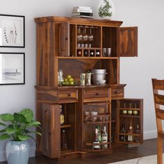 a wooden cabinet filled with lots of bottles and glasses next to a potted plant