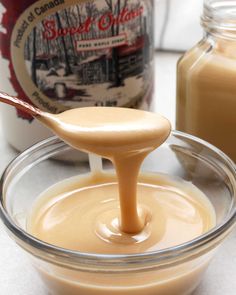 a spoon full of caramel sauce in a glass bowl next to a jar of peanut butter