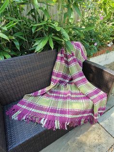 a purple and green plaid blanket sitting on top of a couch next to plants in a garden