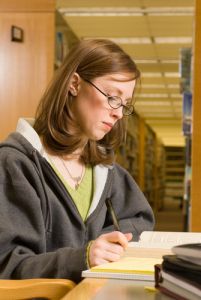 a woman sitting at a table with a book and pen in her hand while writing