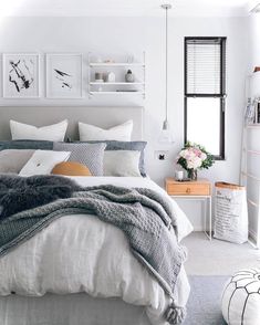 a bedroom with white walls and grey bedding, pillows and blankets on the bed