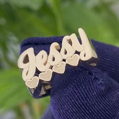 Add a touch of elegance to your look with our personalized cursive name ring. Crafted from solid 10k or 14k gold in yellow, rose, or white, it features a stylish cursive font and hearts as an underline to the name. Metal: 10k or 14k GoldRing Size: Choose your size in drop down optionHeight: 9mm with HeartsProduction Time: 2-3 Weeks Made to order, please add your custom name. The heart underline will adjust based on the spelling of your name. Please contact us for special pricing on additional si West Indian Bangles, Ring With Heart, Picture Pendant, Name Ring, Cursive Font, Name Rings, Bangles Indian, Name Jewelry, Kids Jewelry