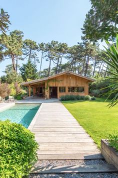 a wooden walkway leading to a pool in the middle of a yard with grass and trees