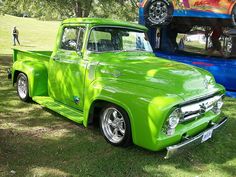 two green trucks parked next to each other in the grass with people standing near them