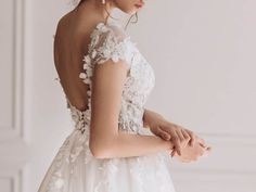 a woman in a white wedding dress with flowers on her shoulder and back, looking off to the side