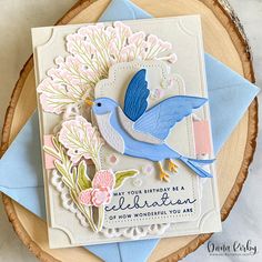 a birthday card with a blue bird on it and flowers in the background, sitting on top of a piece of wood