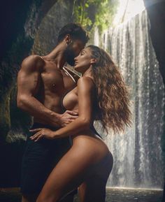 a man and woman standing in front of a waterfall with their arms around each other