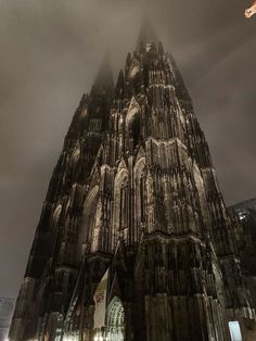 a very tall cathedral towering over a city under a cloudy sky at night with lights on